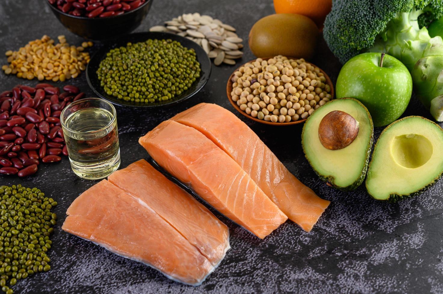 Legumes, broccoli, fruit, and salmon on a black cement background photo