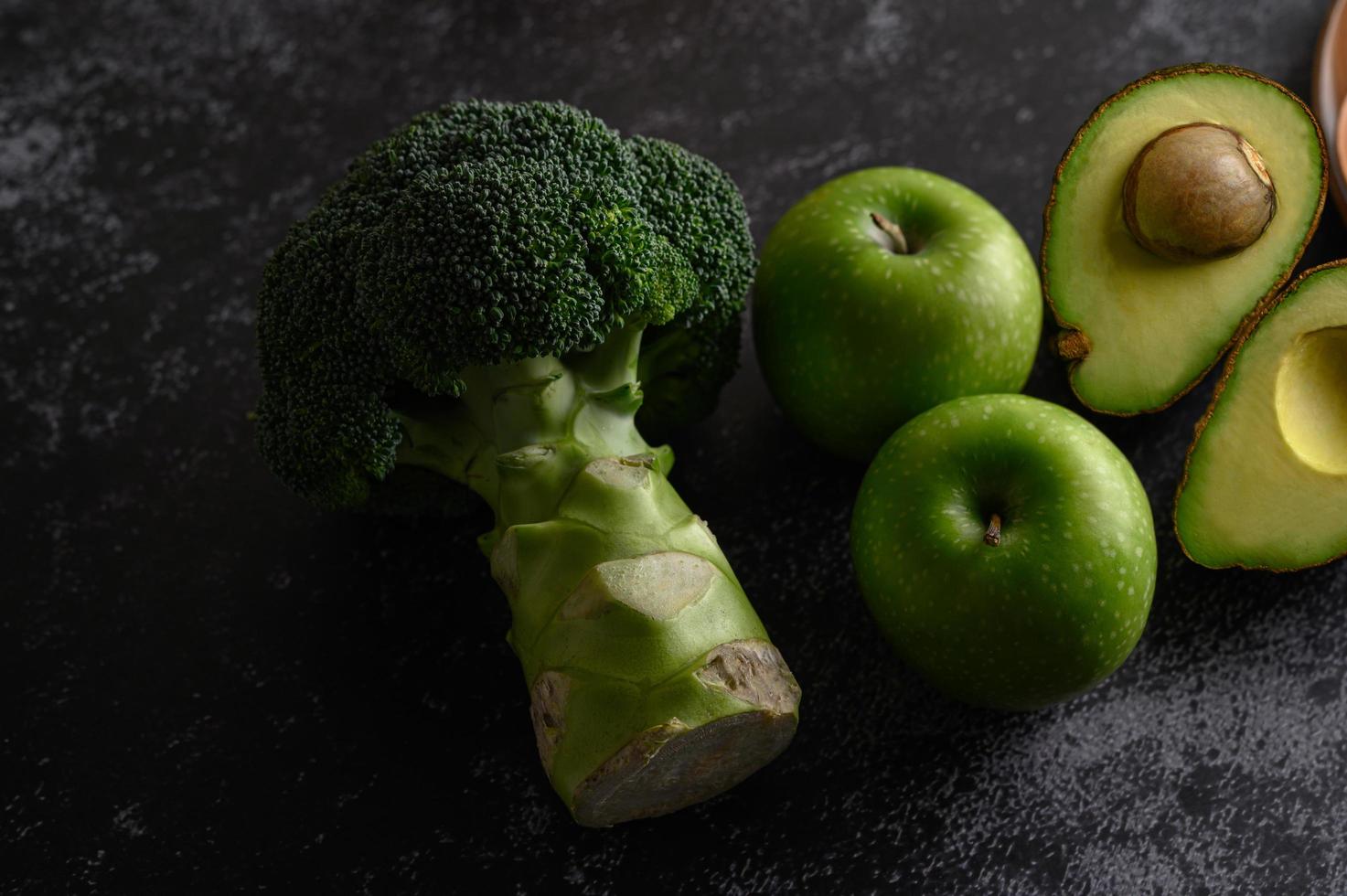 Broccoli, apple and avocado on a black cement floor background photo