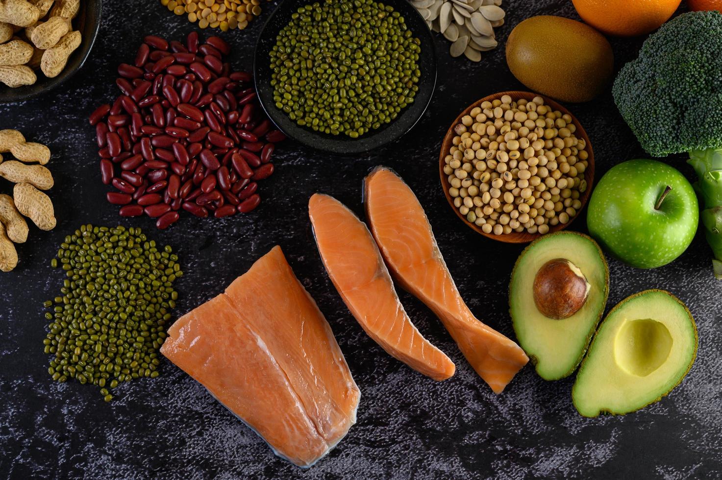 Legumes, broccoli, fruit, and salmon on a black cement background photo