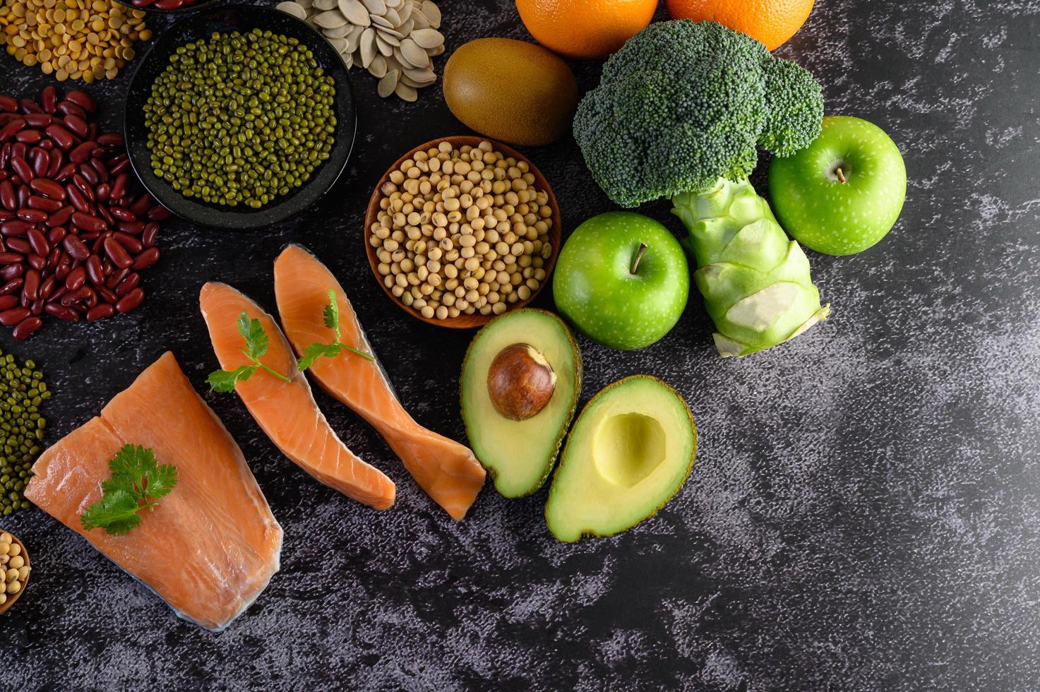 Legumes, broccoli, fruit, and salmon on a black cement background photo