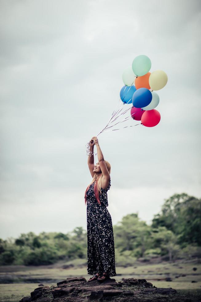 Mujer joven sosteniendo globos de colores en la naturaleza foto