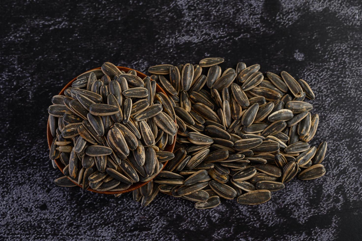Sunflower seeds in a wooden bowl on black surface photo