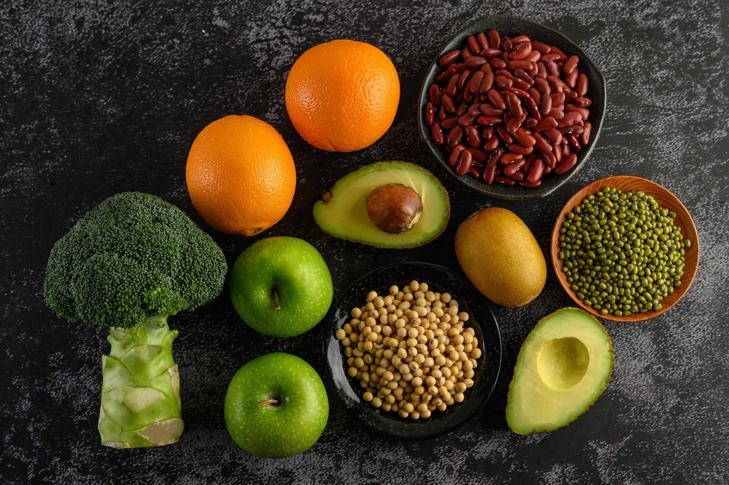 Broccoli, apple, orange, kiwi, avocado and beans on a black cement floor background photo