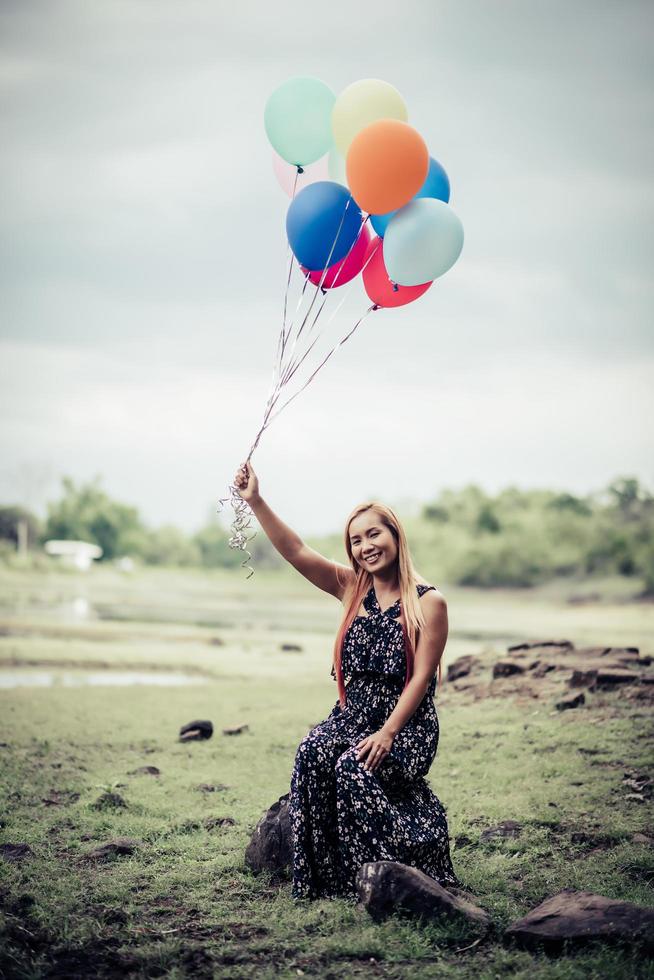 Mujer joven sosteniendo globos de colores en la naturaleza foto