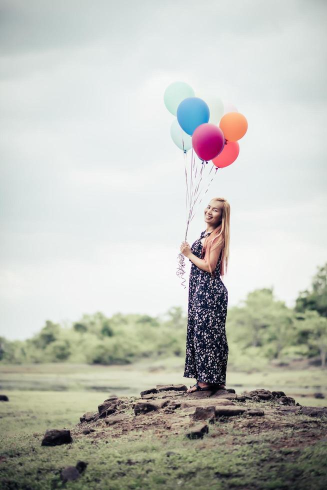 Mujer joven sosteniendo globos de colores en la naturaleza foto