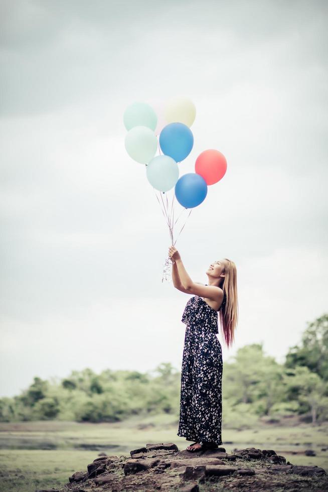 Mujer joven sosteniendo globos de colores en la naturaleza foto