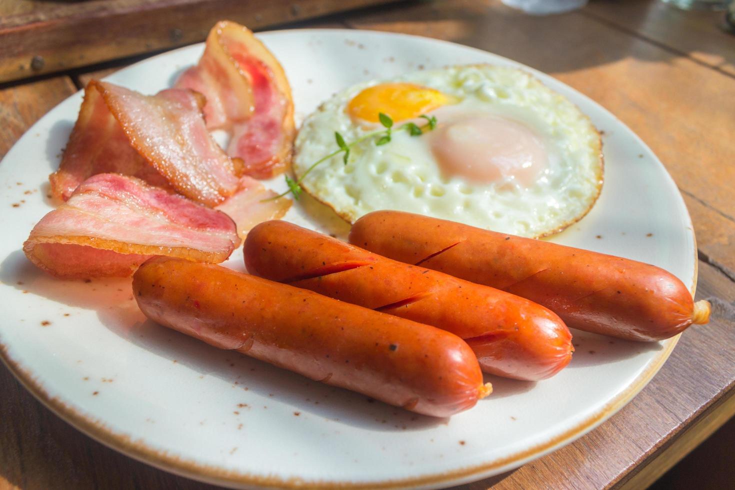 tocino, huevos fritos y salchichas en placa blanca y mesa de madera foto