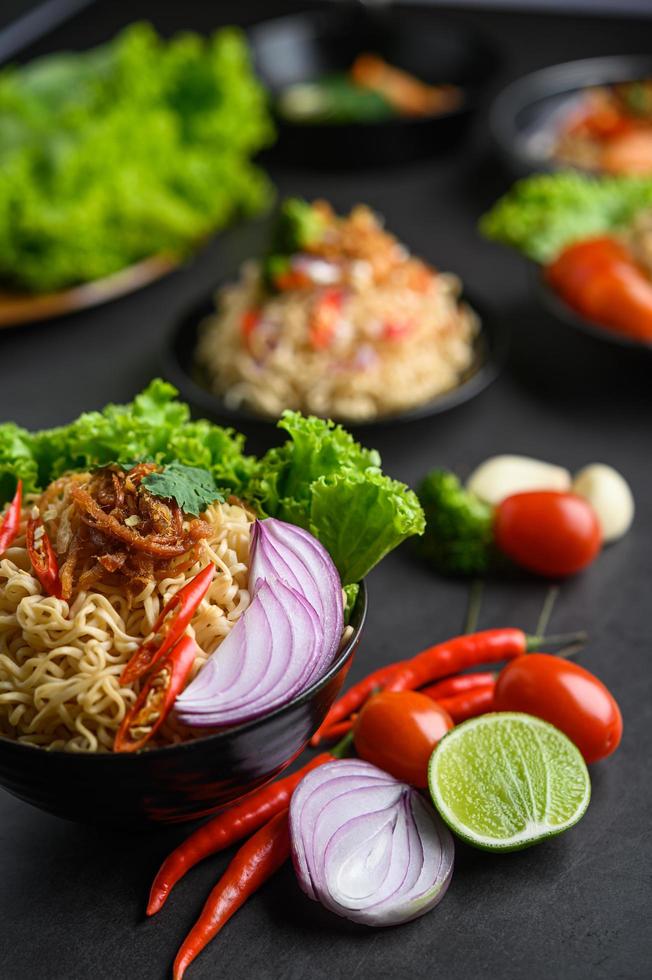 Fideos en un recipiente con ingredientes sobre fondo de cemento negro foto