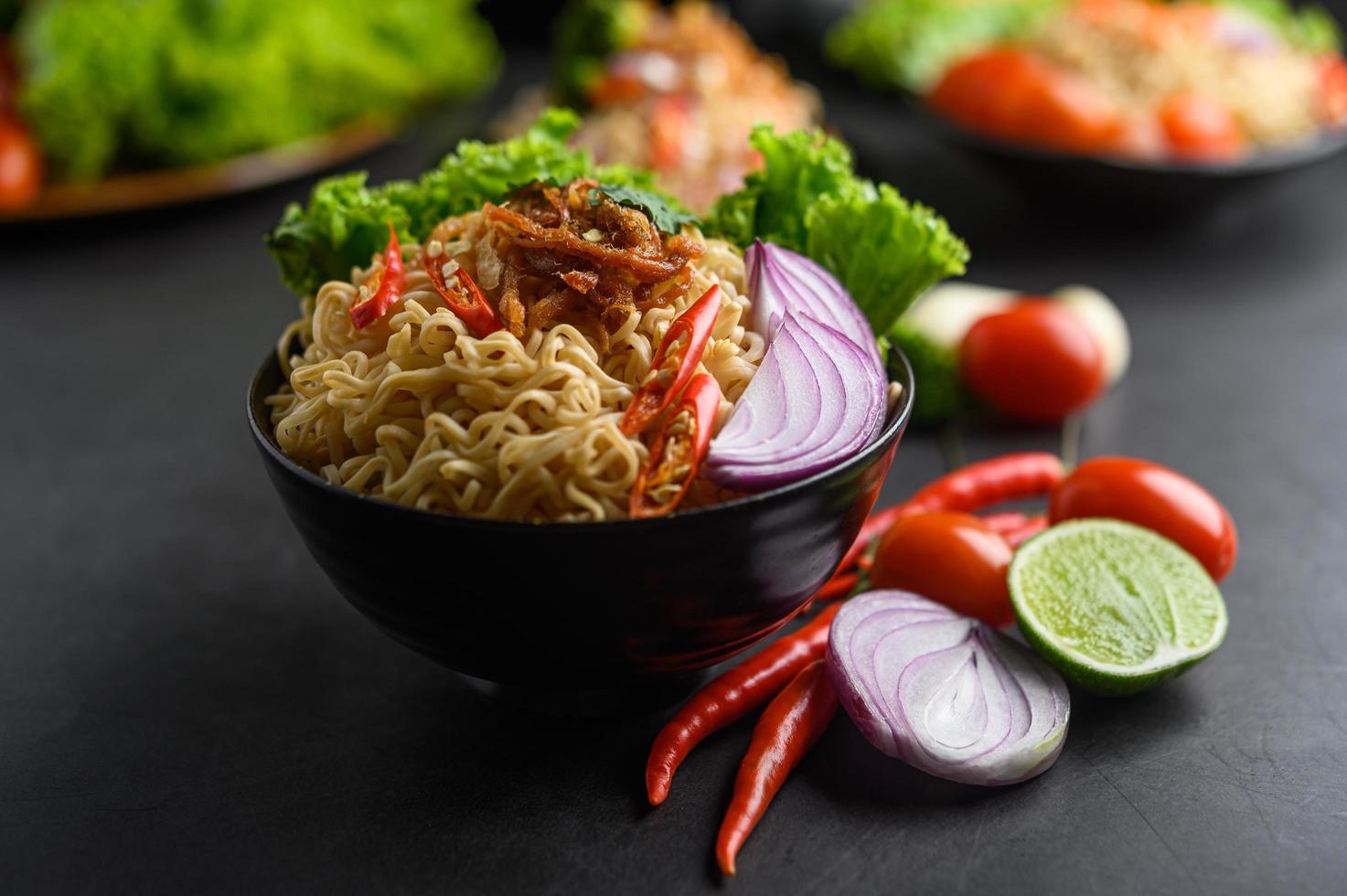 Noodles in a bowl with ingredients on black cement background photo