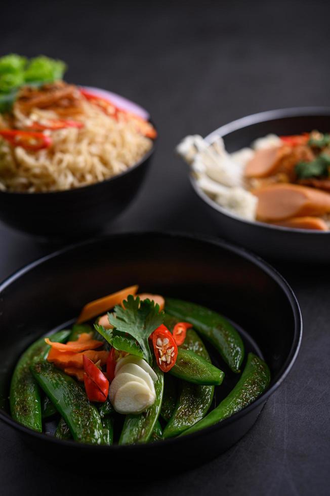 Stir-fried peas in a pan and noodles with ingredients on black background photo