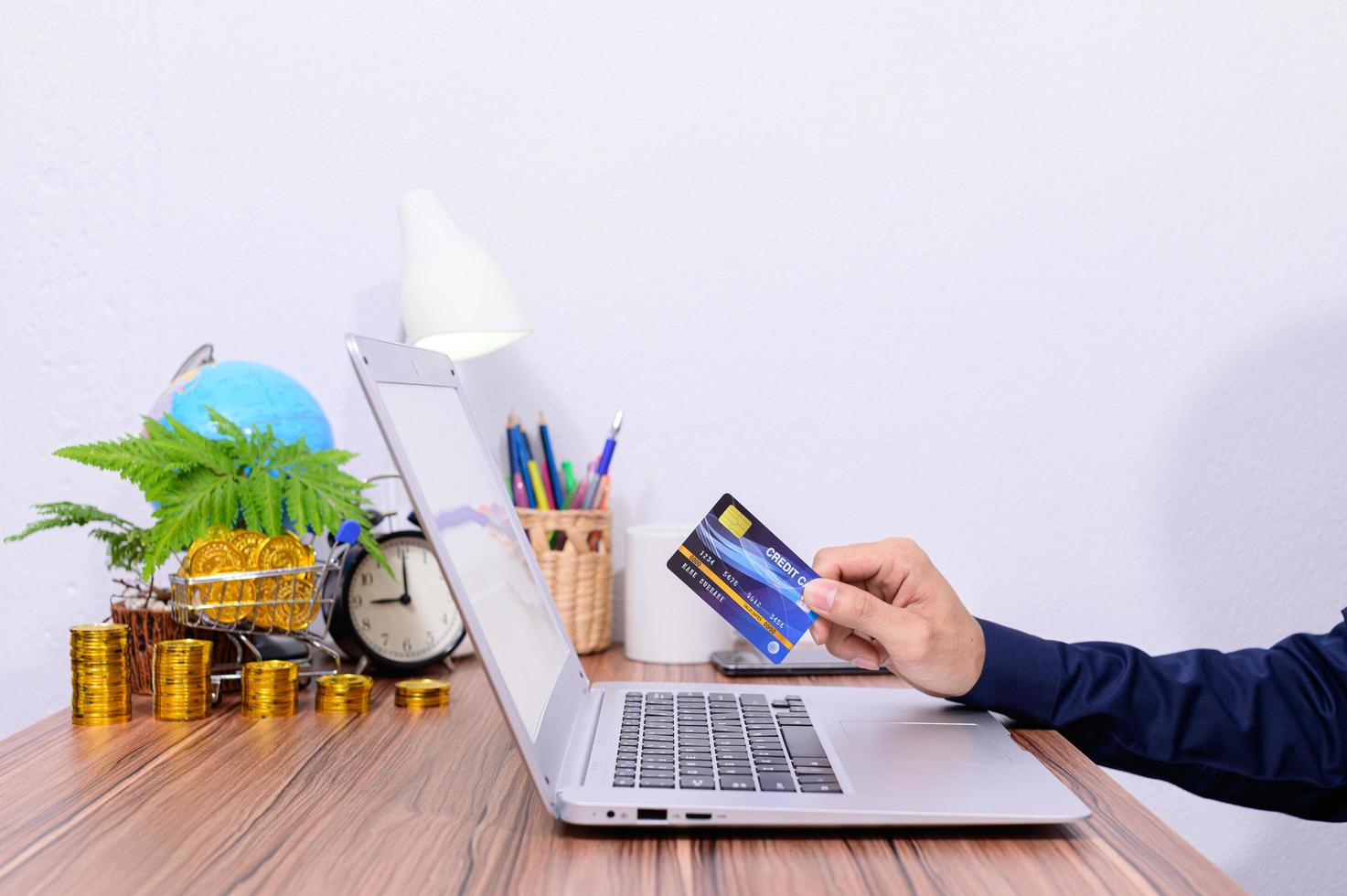 Hombre sujetando una tarjeta de crédito azul mientras está en una computadora portátil foto