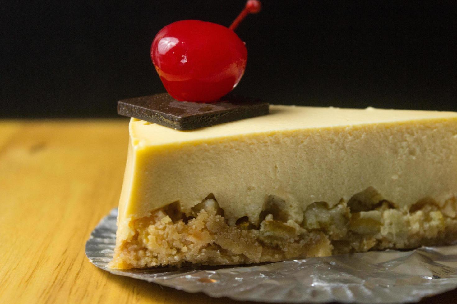 Rebanada de tarta de queso con chocolate y cereza sobre mesa de madera foto