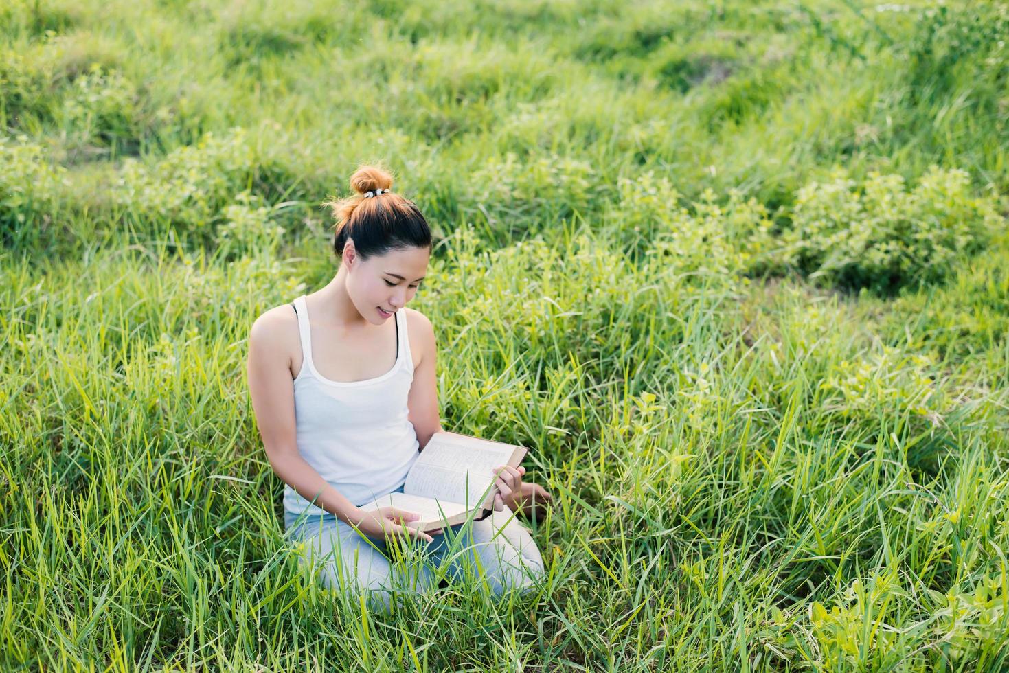 Joven y bella mujer asiática sentada y leyendo un libro en la pradera foto