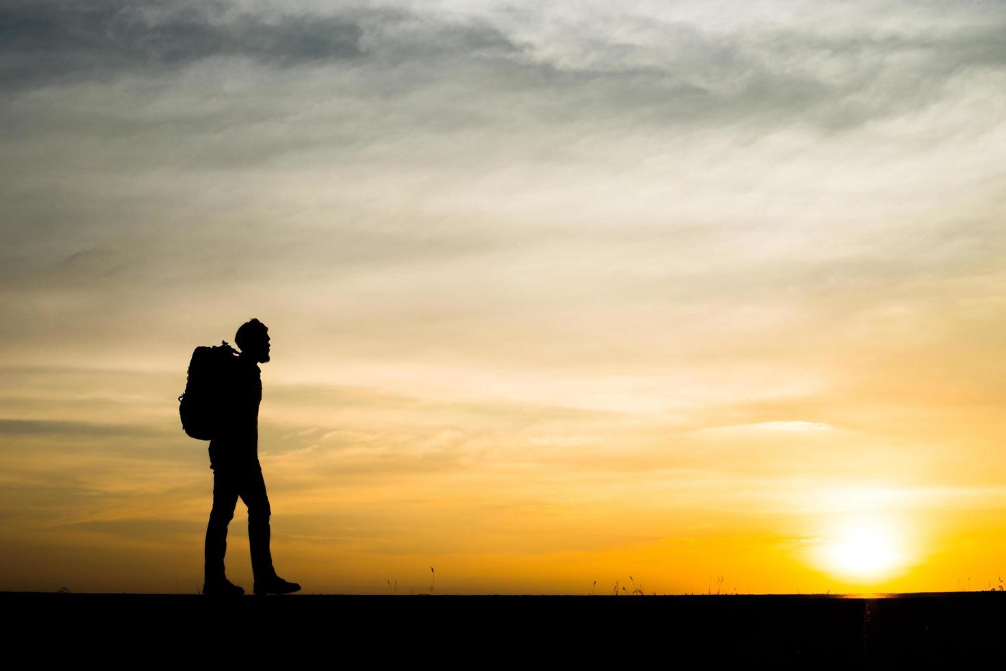 Silhouette of a young backpacker man walking during sunset photo