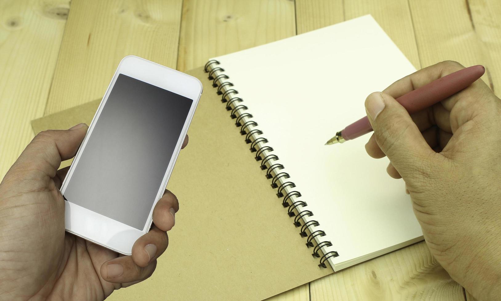 Person using phone and writing in notebook photo