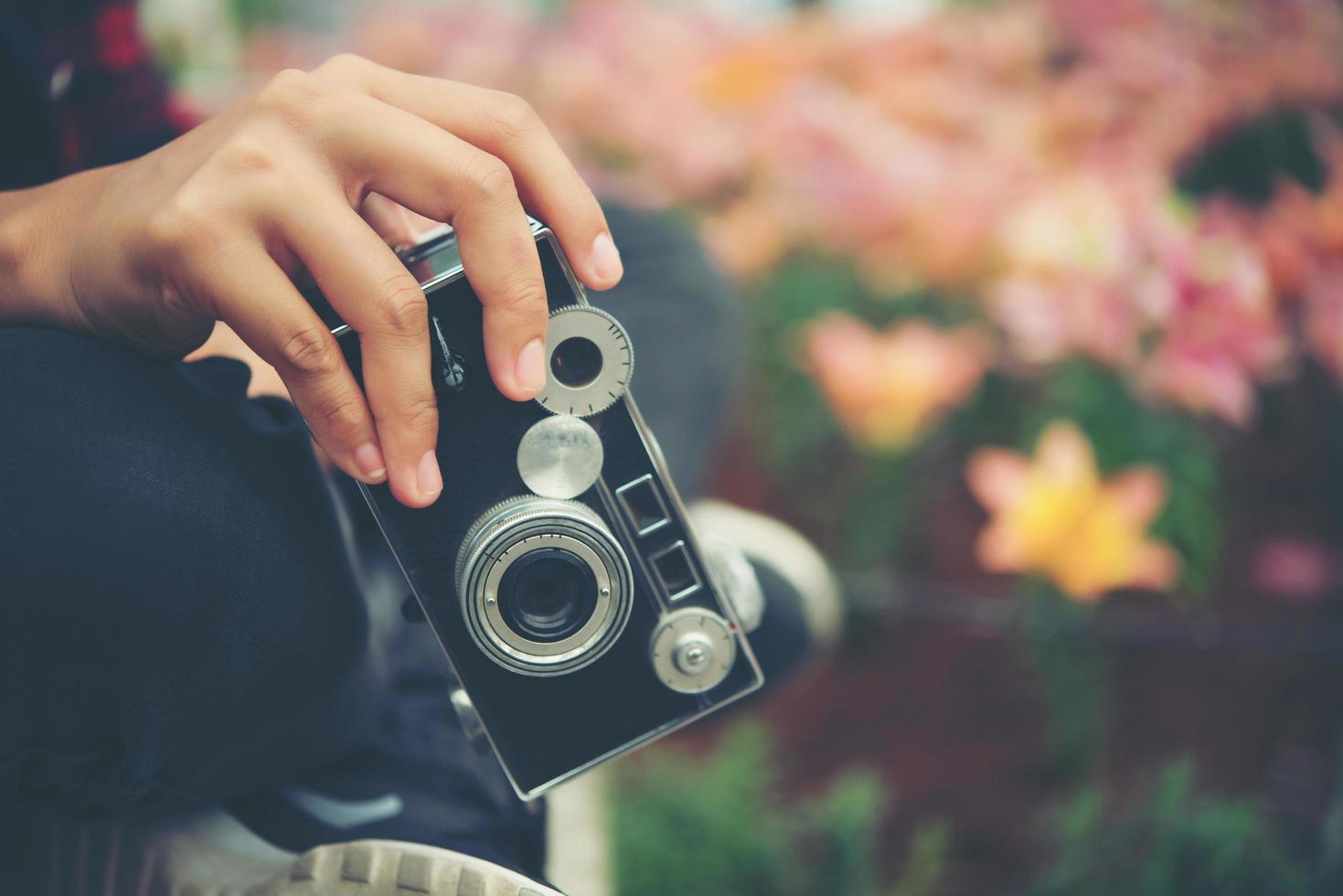 Primer plano de la mano de una mujer con una cámara vintage disparando flores en un jardín. foto