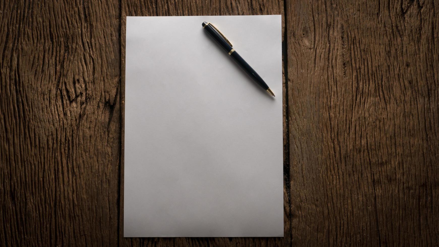 Blank sheet of paper and pen on a wooden table photo