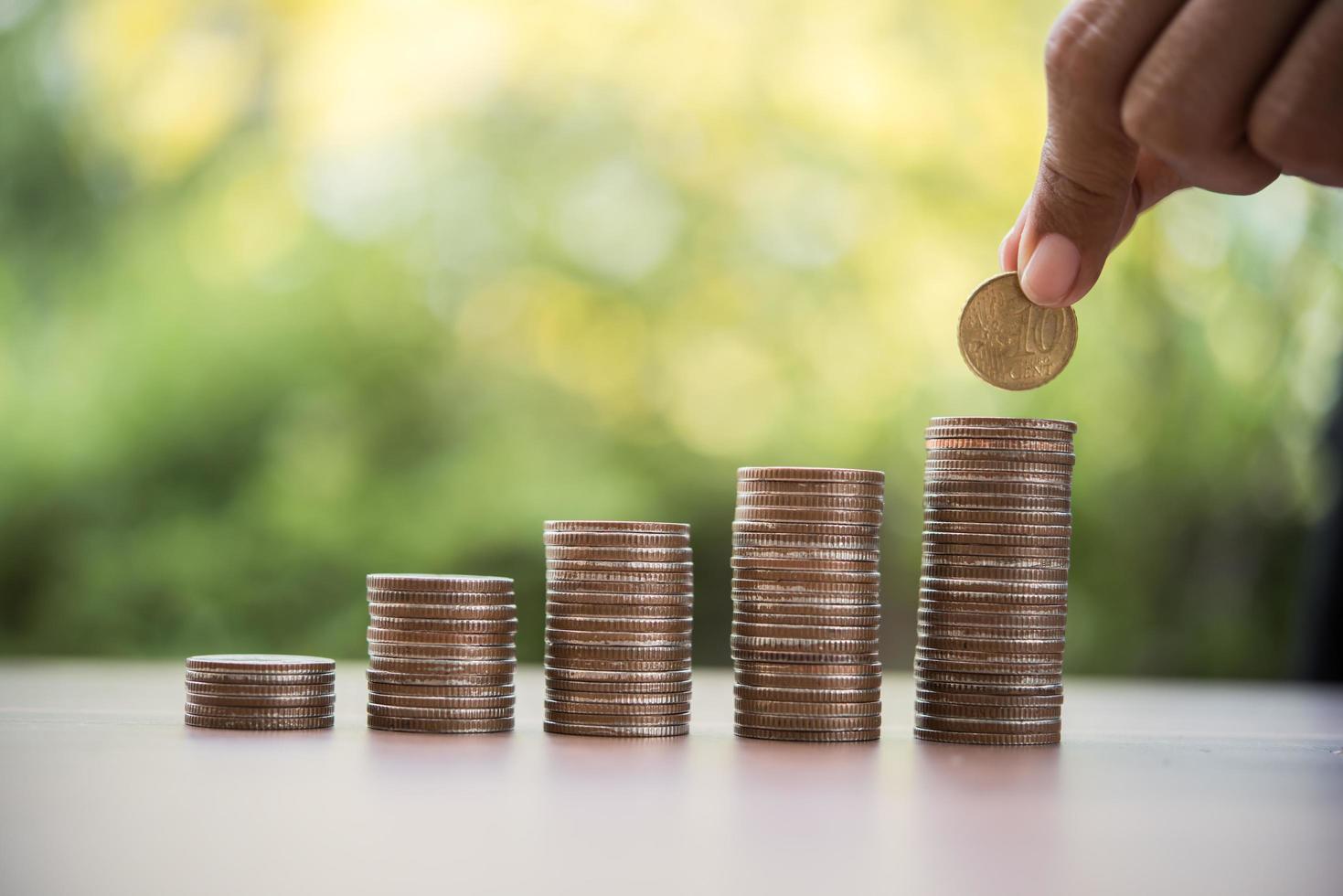 Manos poniendo pilas de monedas de dinero juntas en la naturaleza foto