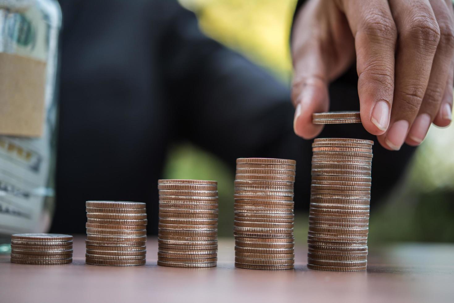 Manos poniendo pilas de monedas de dinero juntas en la naturaleza foto