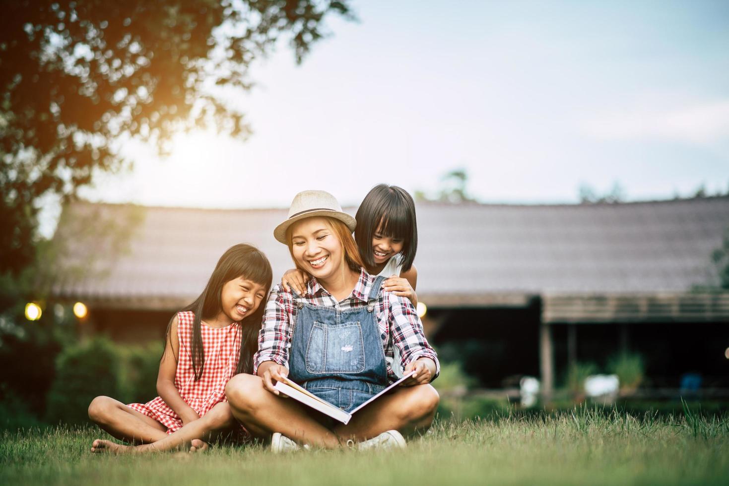 Madre contando una historia a sus dos pequeñas hijas en el jardín de la casa. foto