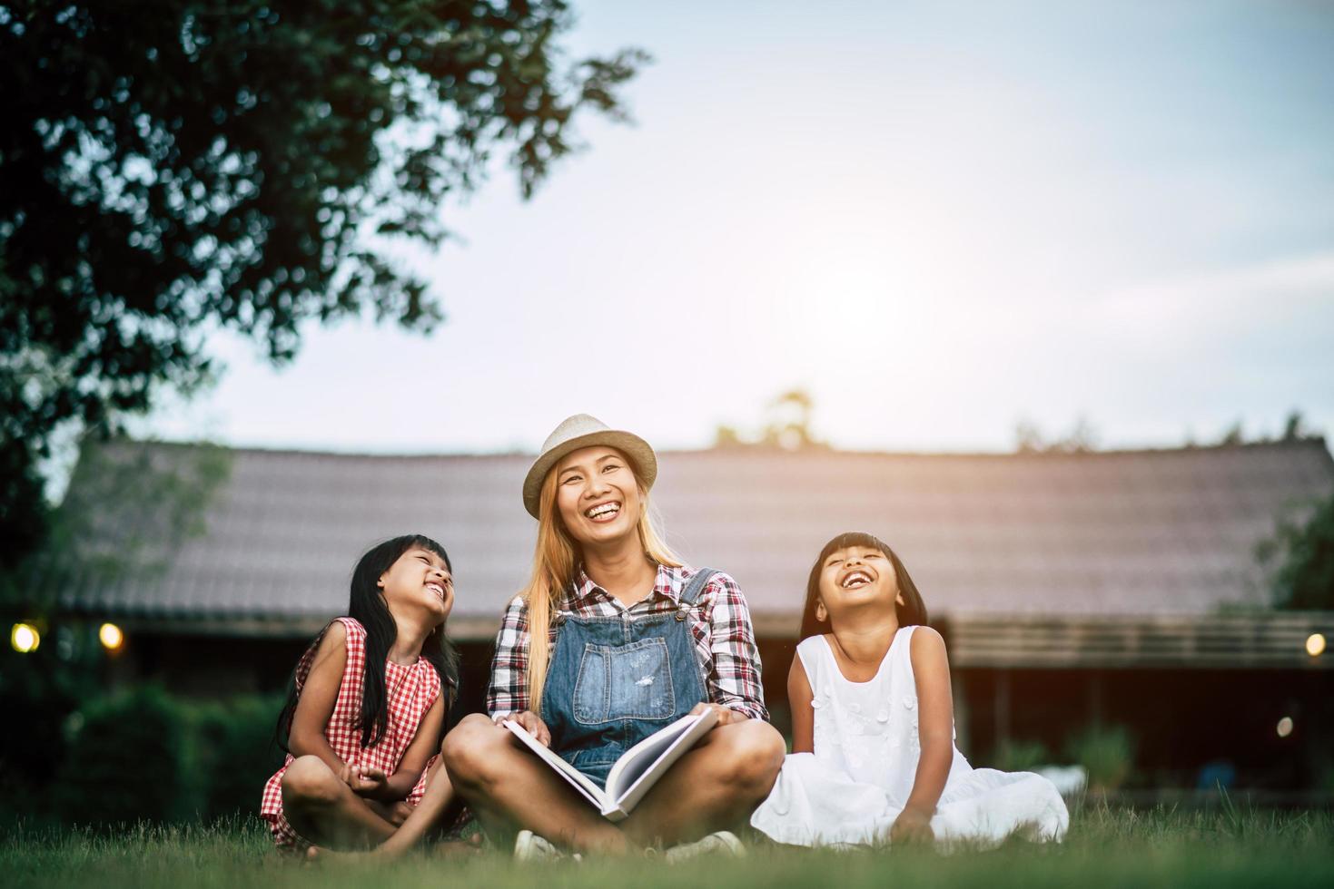 Madre contando una historia a sus dos pequeñas hijas en el jardín de la casa. foto