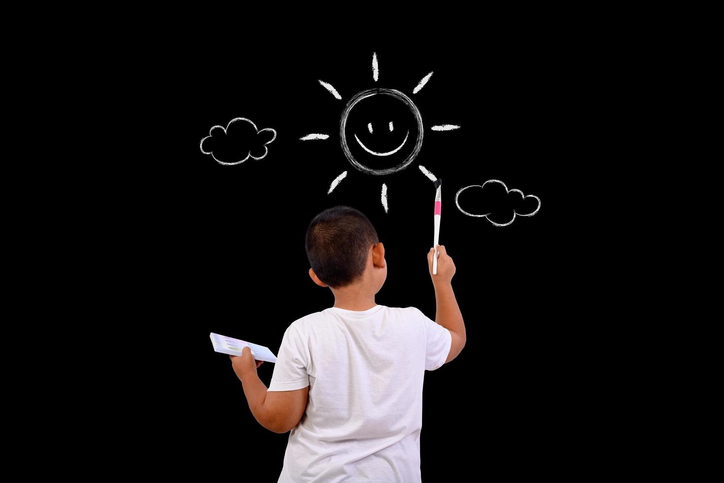 A boy draws the sky and the sun on a chalkboard photo