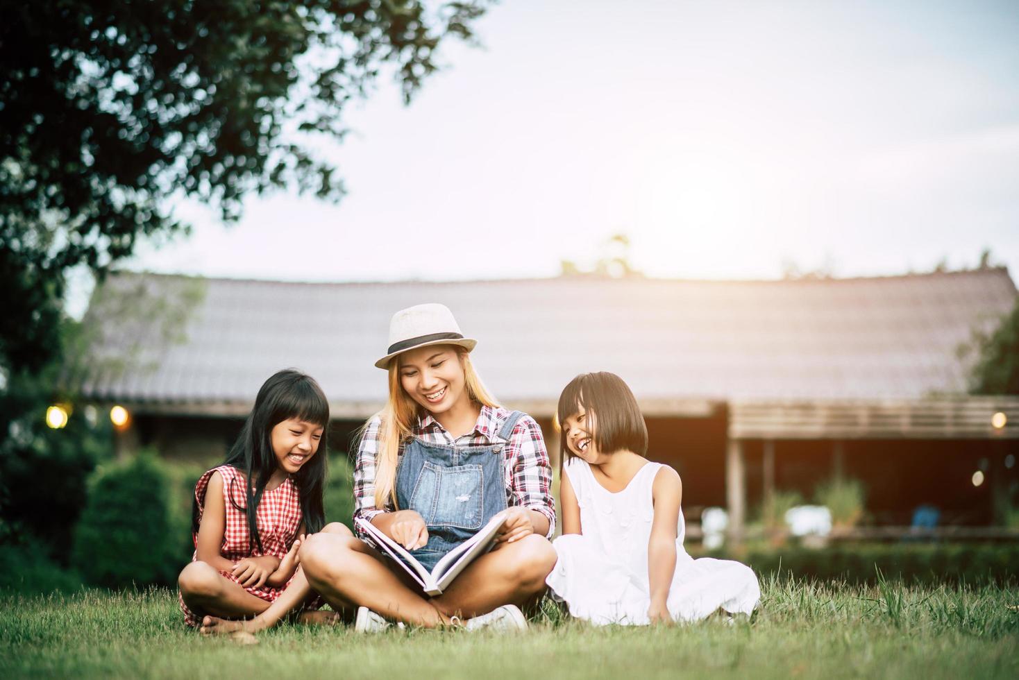 Madre contando una historia a sus dos pequeñas hijas en el jardín de la casa. foto