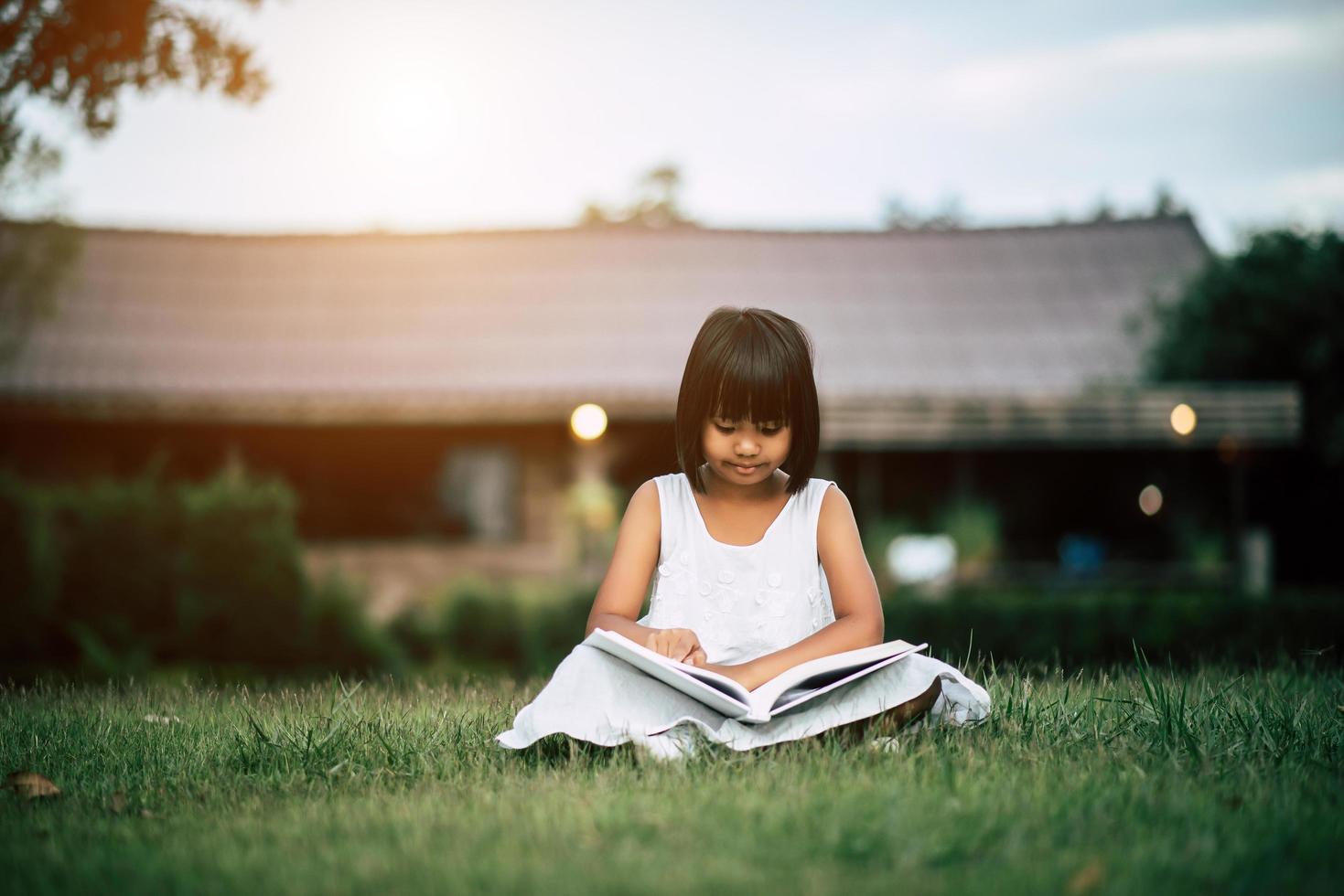 Little girl reading a book in her house garden outside photo