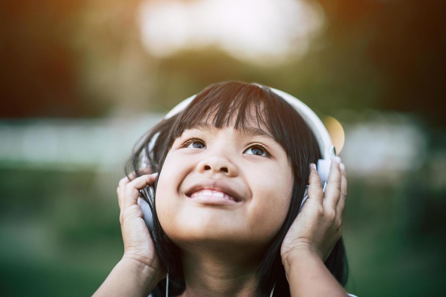 niña escuchando música en el parque con auriculares foto