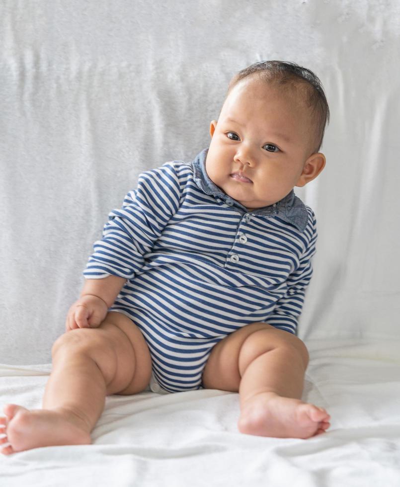 A baby learning to sit on a white bed photo