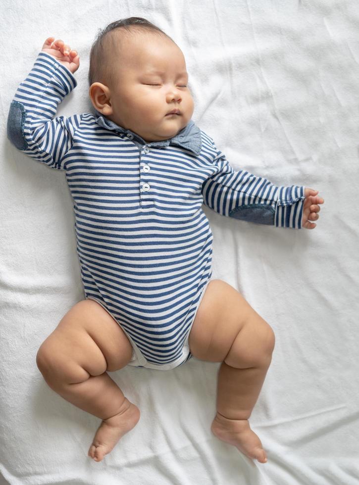 A baby boy in a striped shirt sleeping in bed photo