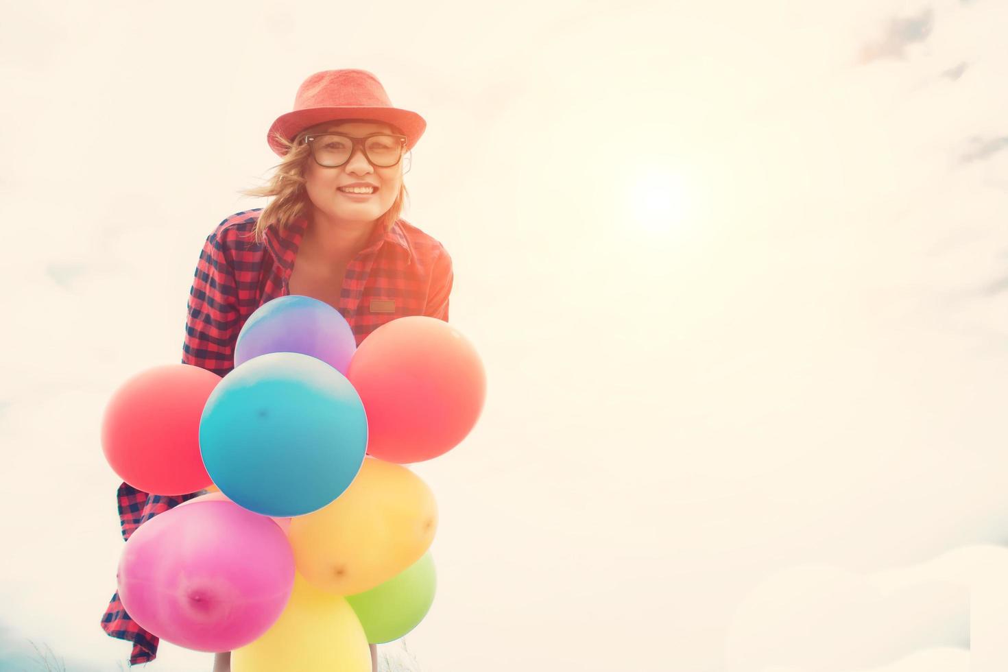 Young hipster woman holding balloons below the sky photo