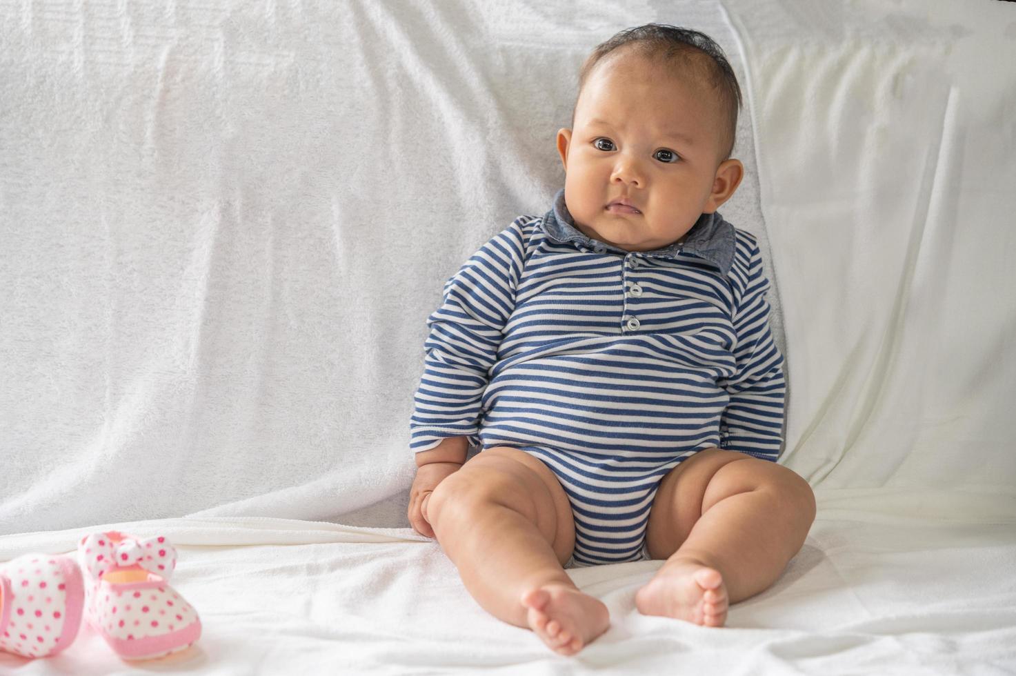 bebé aprendiendo a sentarse en una cama blanca foto