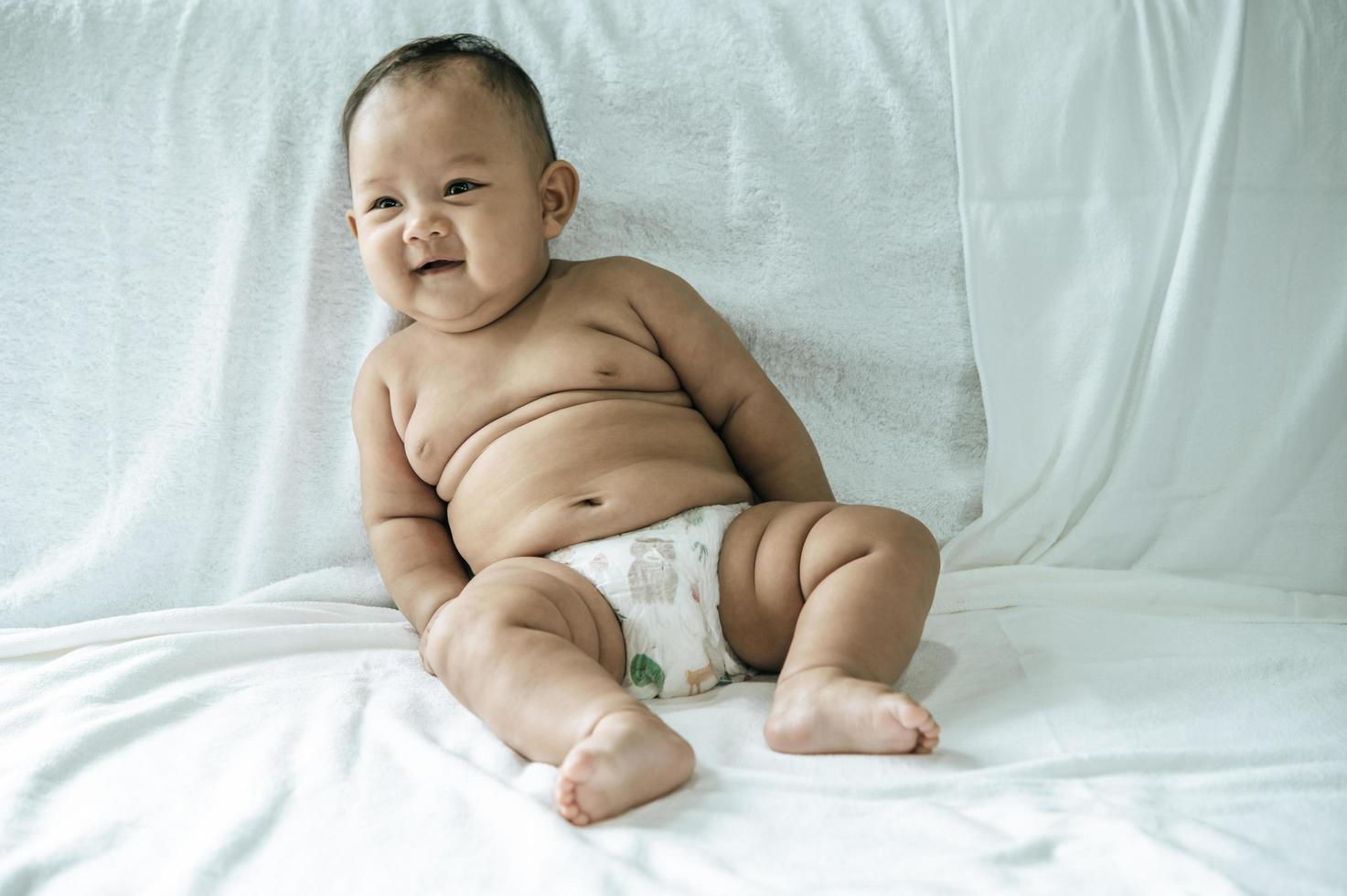 A baby learning to sit on a white bed photo