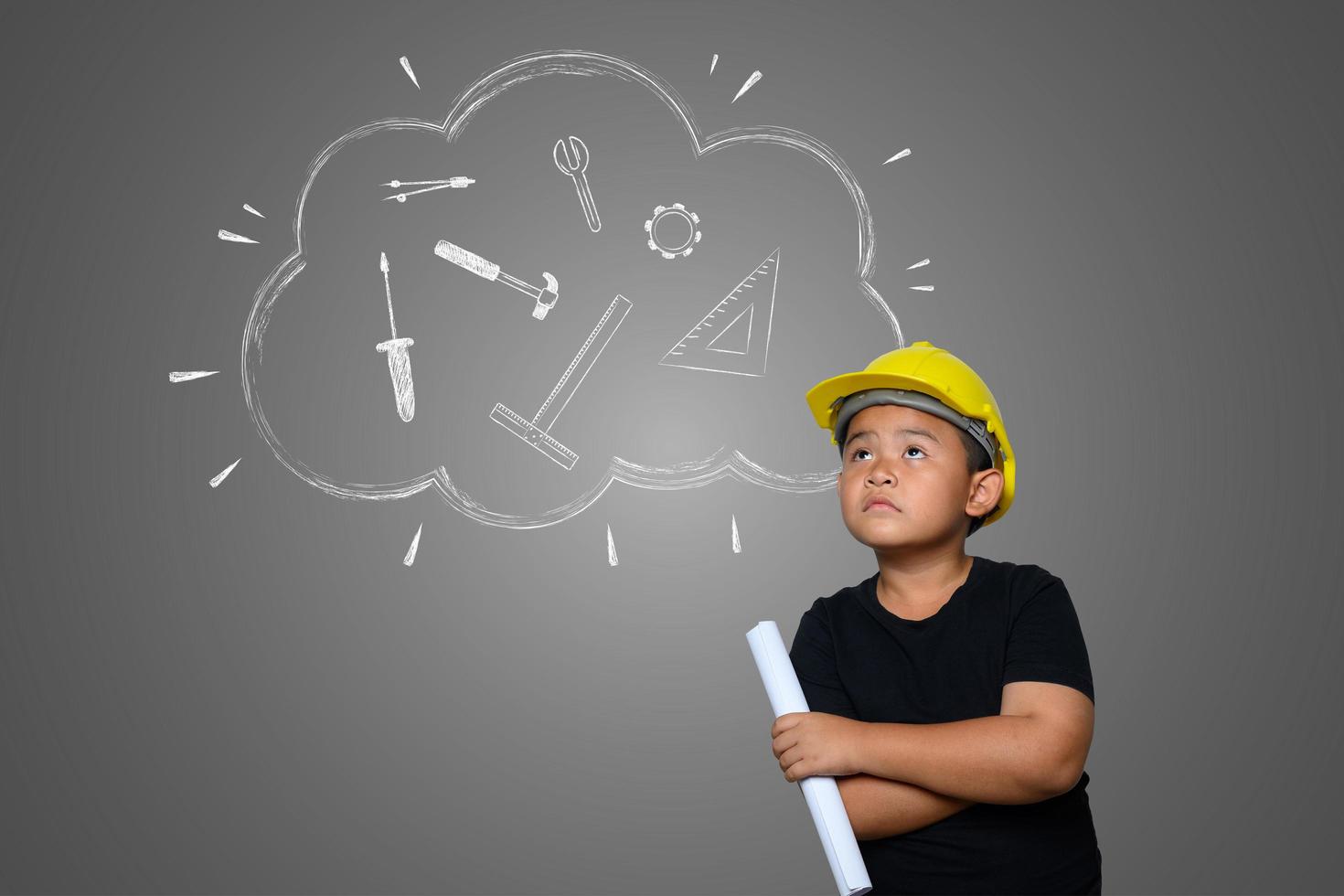 A boy wearing a yellow engineer hat and a house plan on blackboard photo