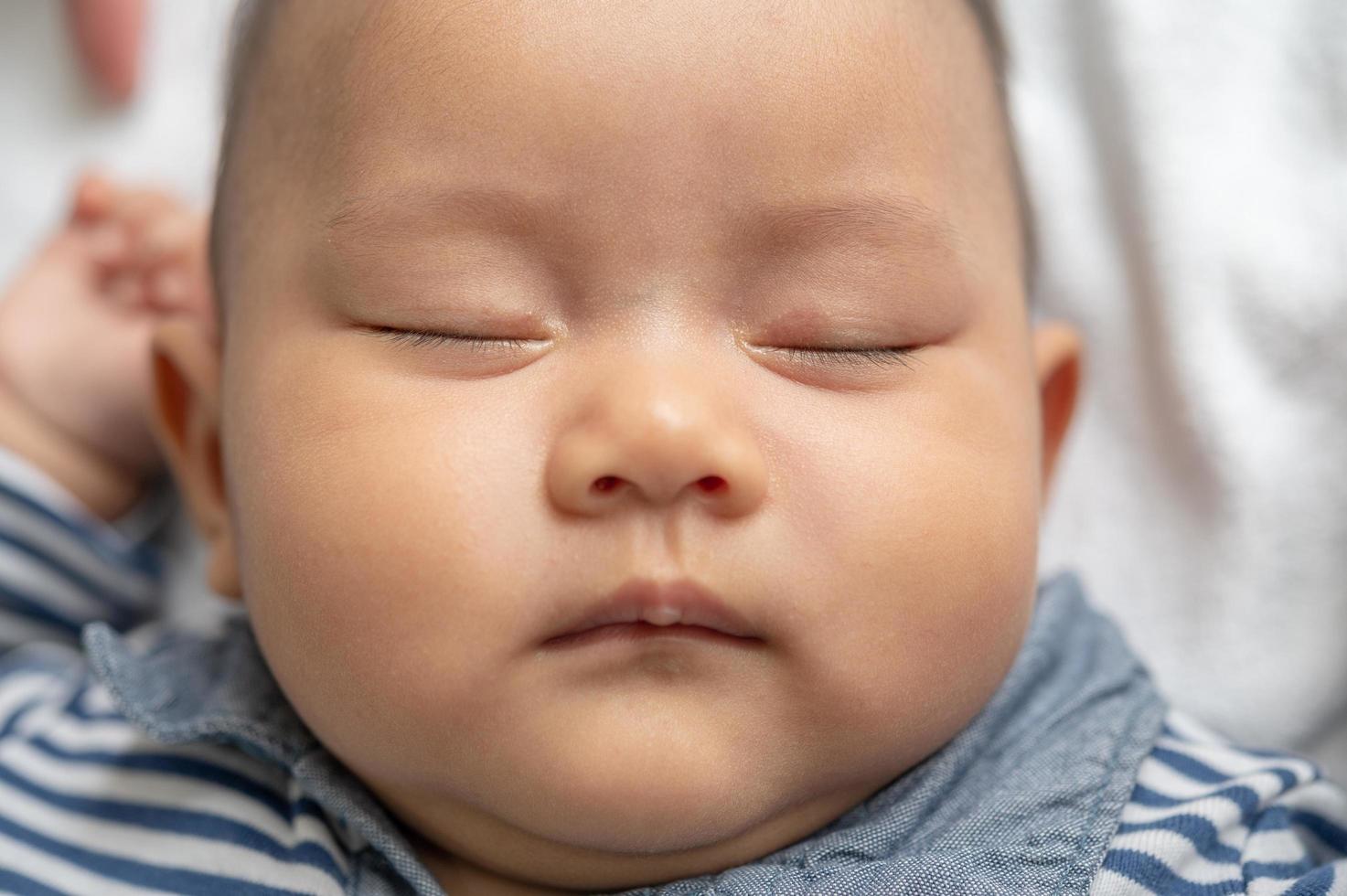 A baby boy in a striped shirt sleeping in bed photo