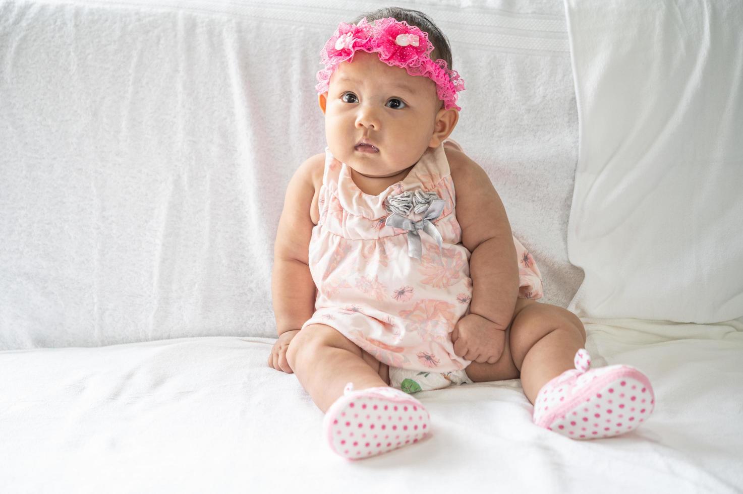 A baby learning to sit on a white bed photo