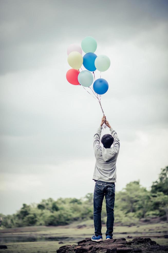 joven sosteniendo globos de colores en la naturaleza foto