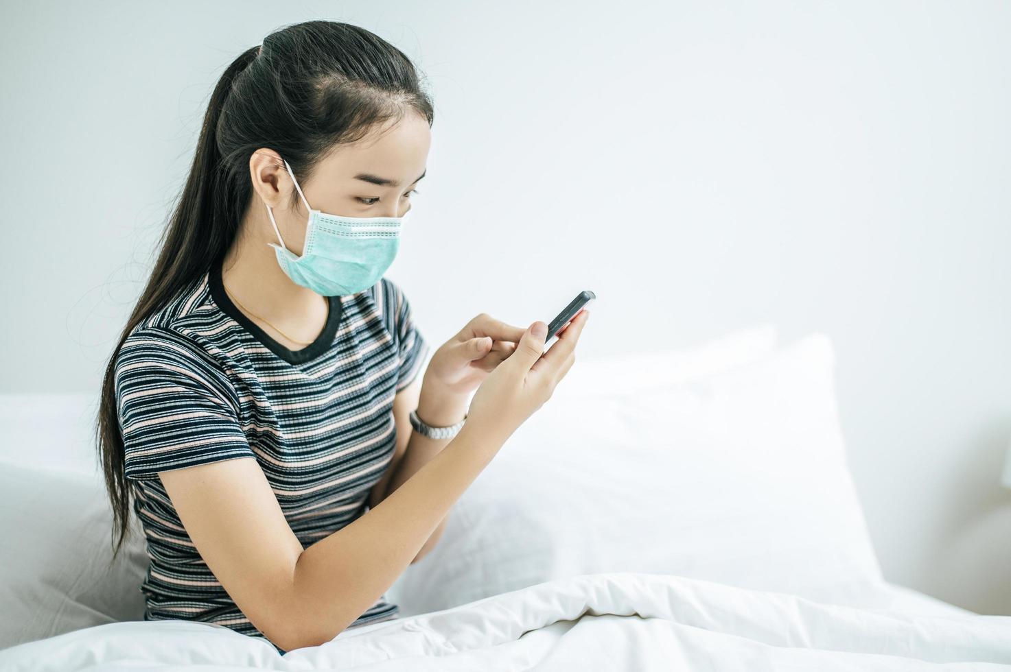 niña con una máscara de saneamiento, camisa a rayas y sosteniendo un teléfono móvil foto