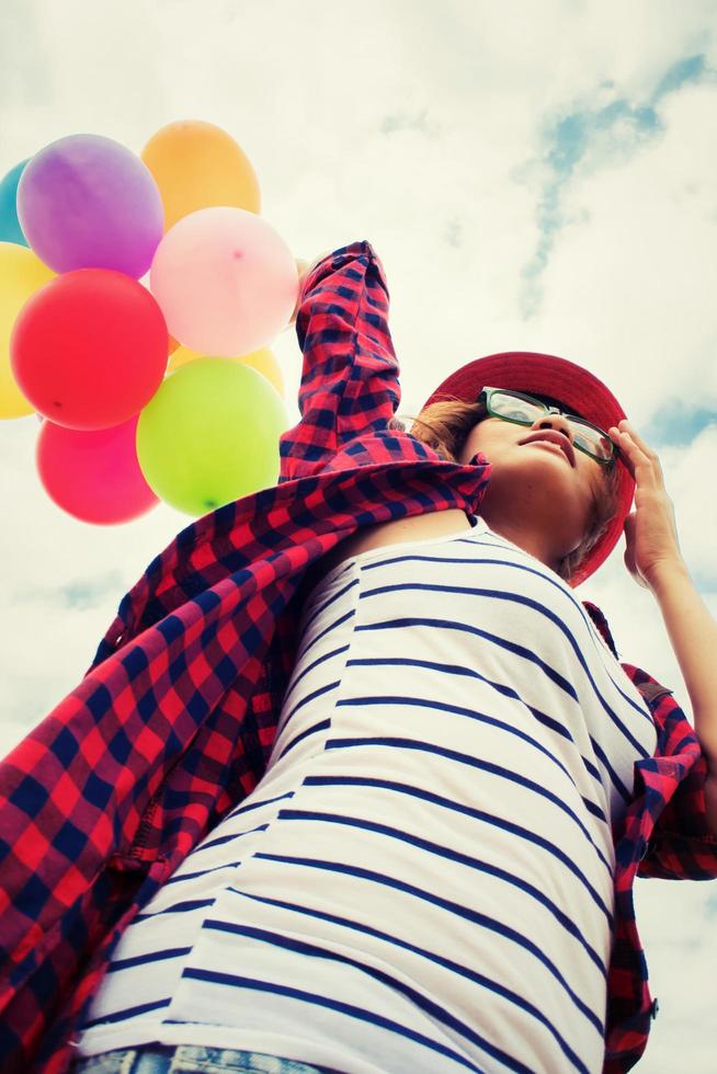 Adolescente sosteniendo globos de colores en el cielo brillante foto