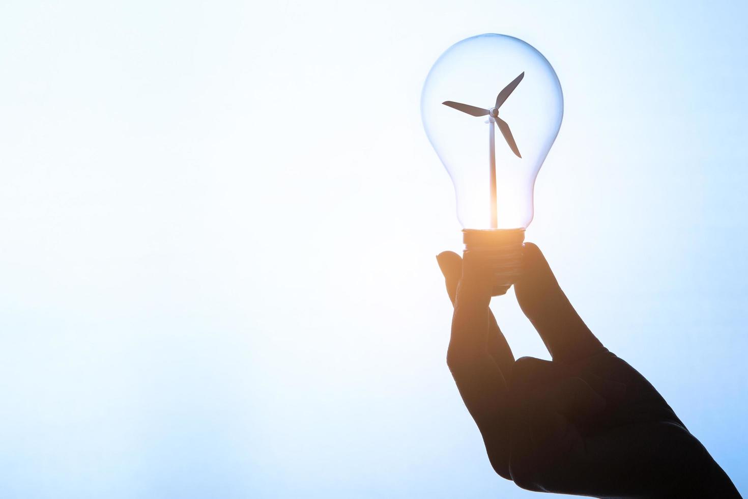 Hand holding lightbulb with wind turbine photo