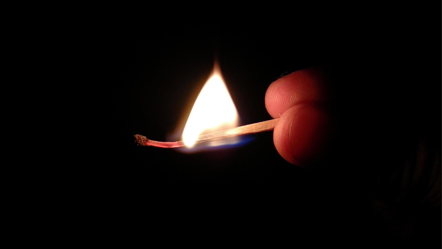 Lit match held between thumb and finger on black background photo