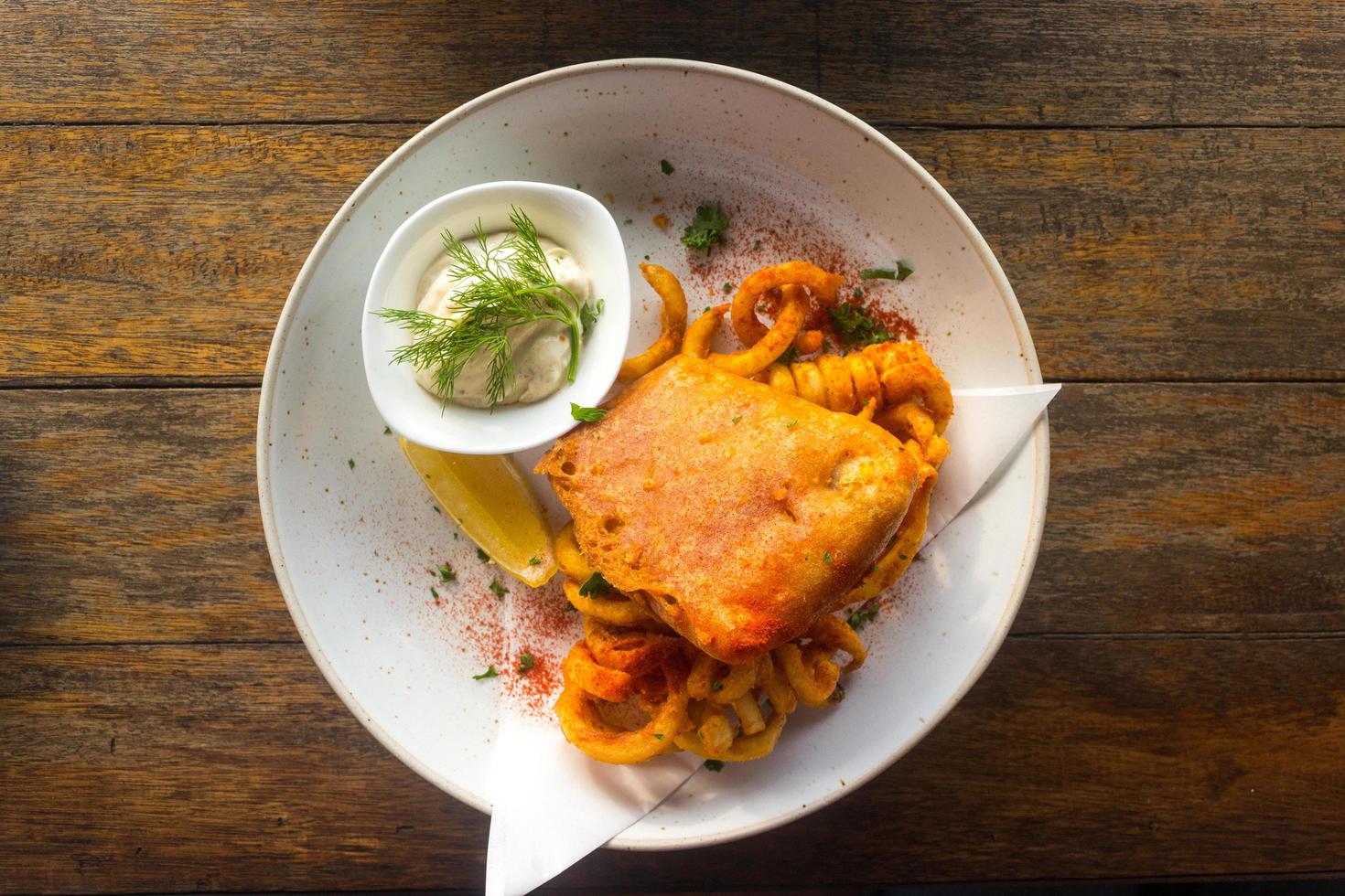 Fish and chips with tartar sauce on white plate and wooden table photo