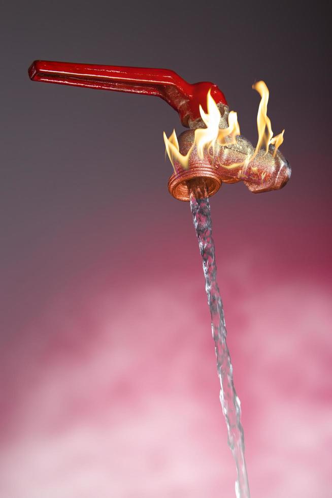 El agua que fluye del grifo con llamas y palanca roja sobre fondo rojo. foto