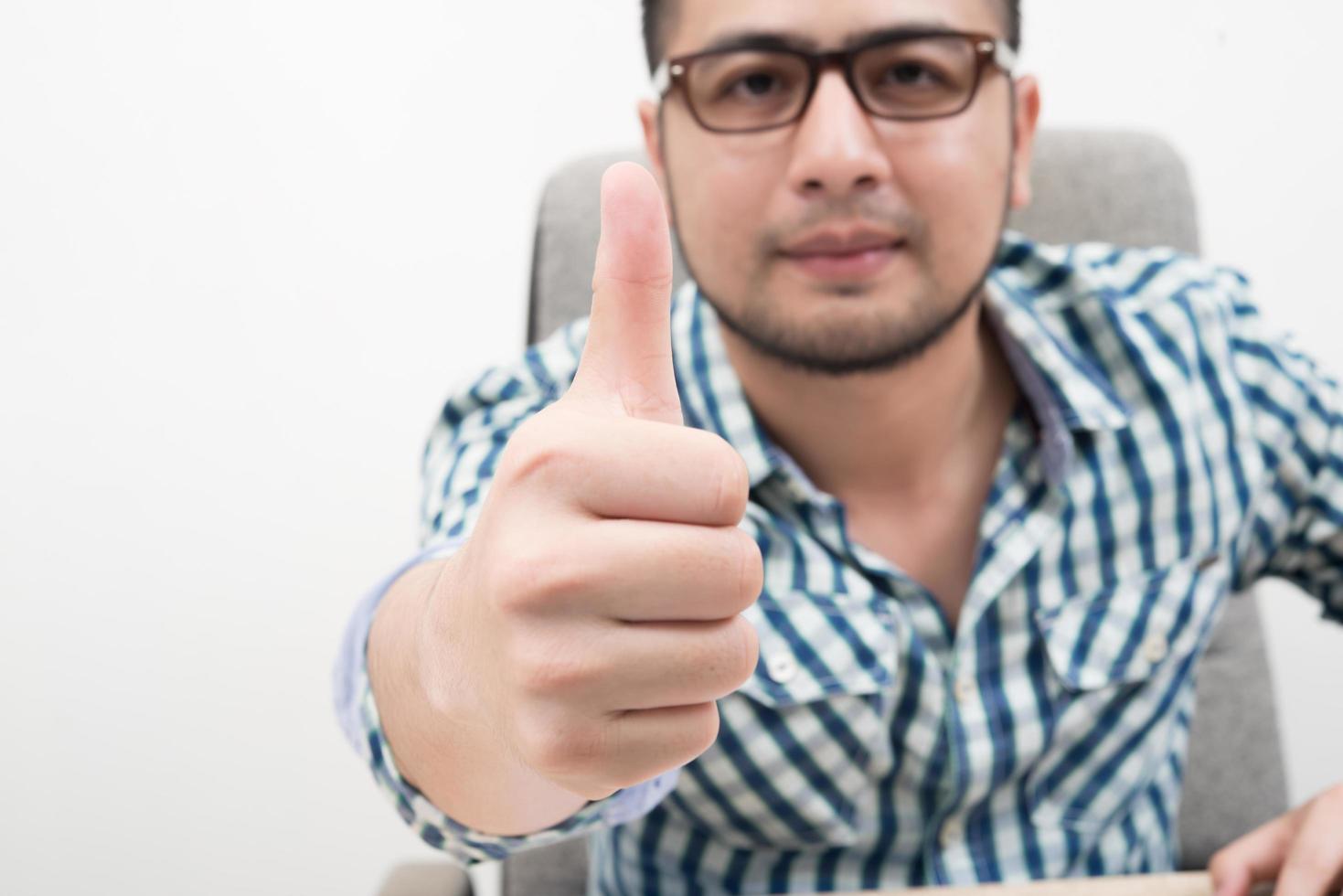 Retrato de joven empresario con Thumbs up sentado en el lugar de trabajo foto