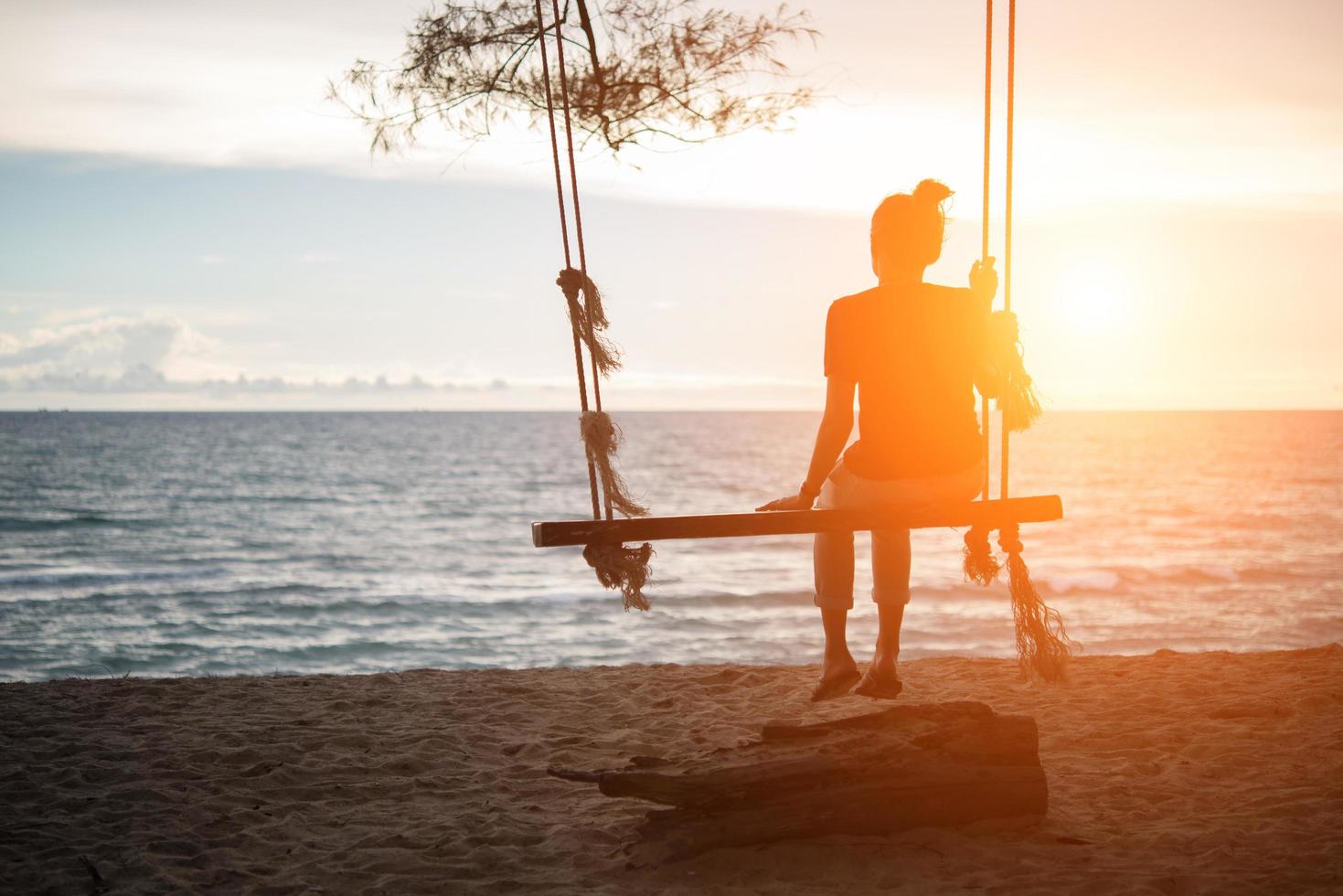 Young woman watching the sunset alone on swing at the beach photo