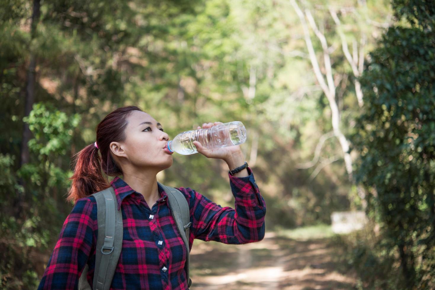 Happy woman tourist with backpack drinking water in nature photo