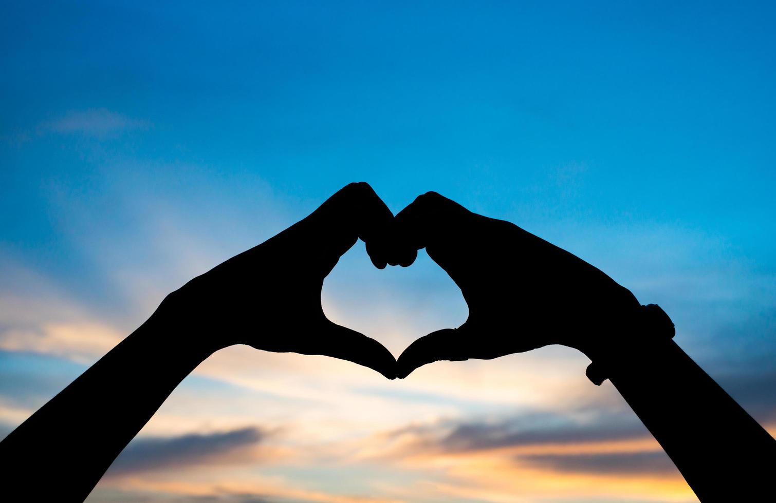 silueta de las manos de una mujer en forma de corazón con amanecer foto