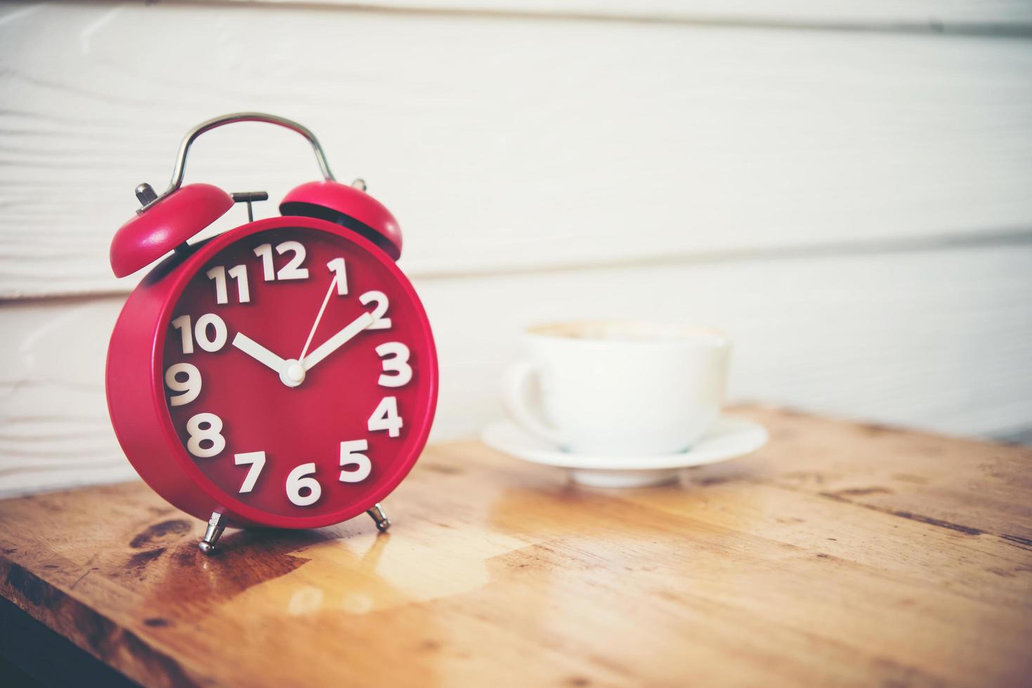 Red alarm clock with coffee on wooden table photo