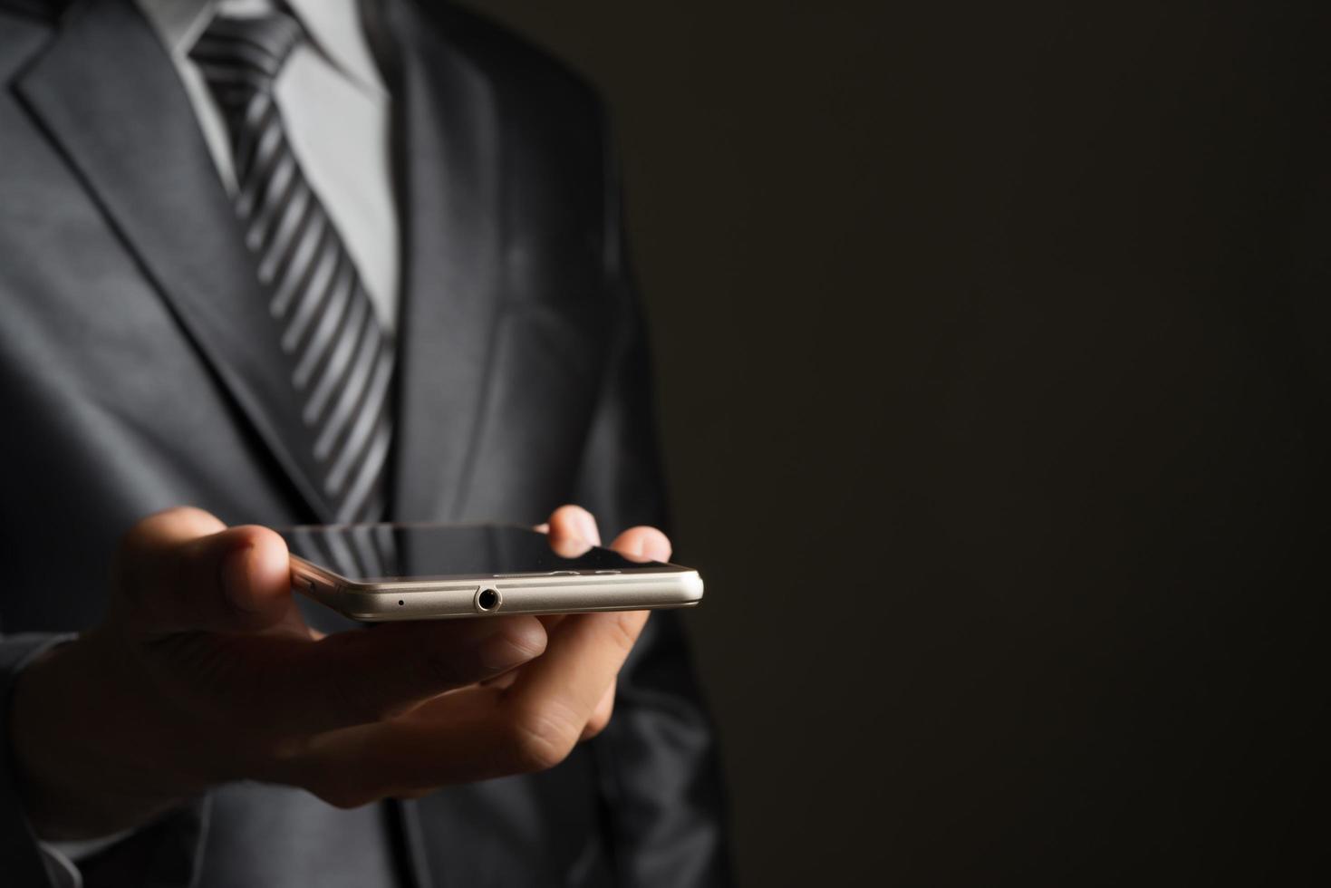 Portrait of a businessman holding smartphone against black background photo